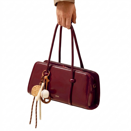 Maroon handbag with keychains held by a hand on a white background